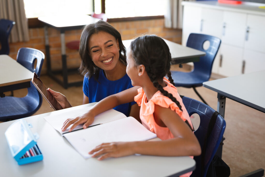 Female teacher with digital tablet teaching a girl in primary school